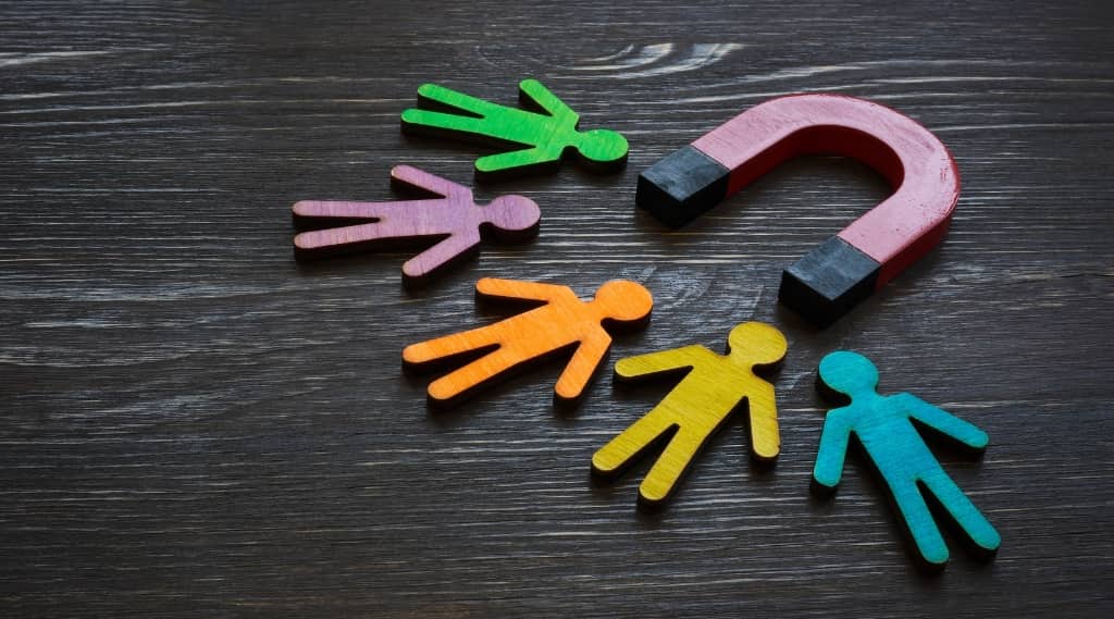 Red horseshoe magnet attracting multicoloured wooden figures, symbolising landing pages that attract customers.